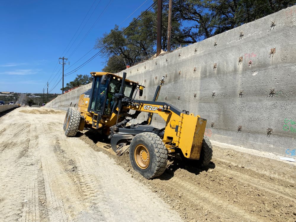 A grader levels the ground near a newly built wall at US 290 near Circle Drive. This work enables crews to shift traffic on US 290, allowing more space for future wall construction along US 290. 